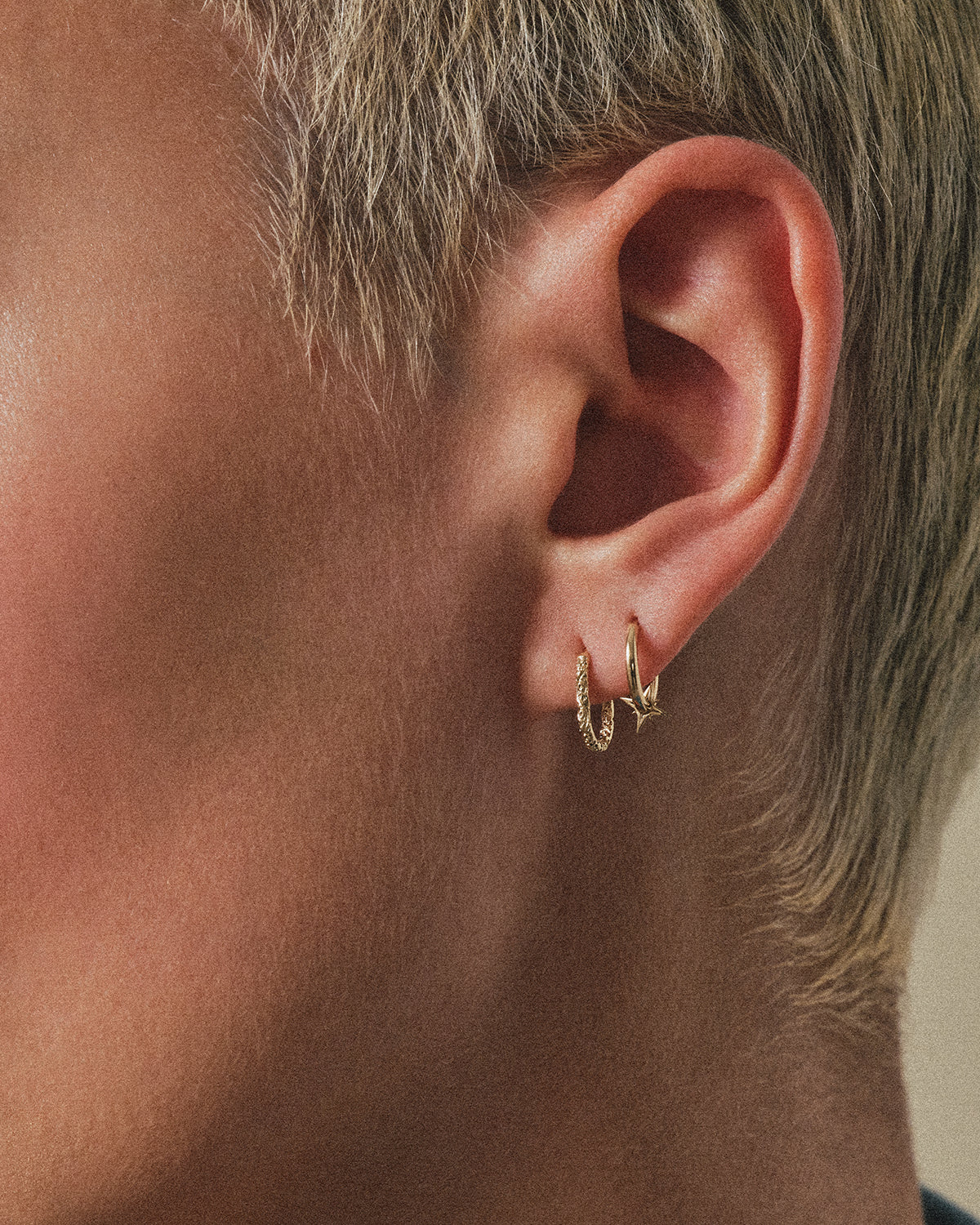 Close-up of an ear wearing gold hoop earrings metier by tomfoolery astra add on oval clicker