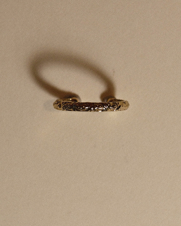 Gold ear cuff with intricate design on a beige background