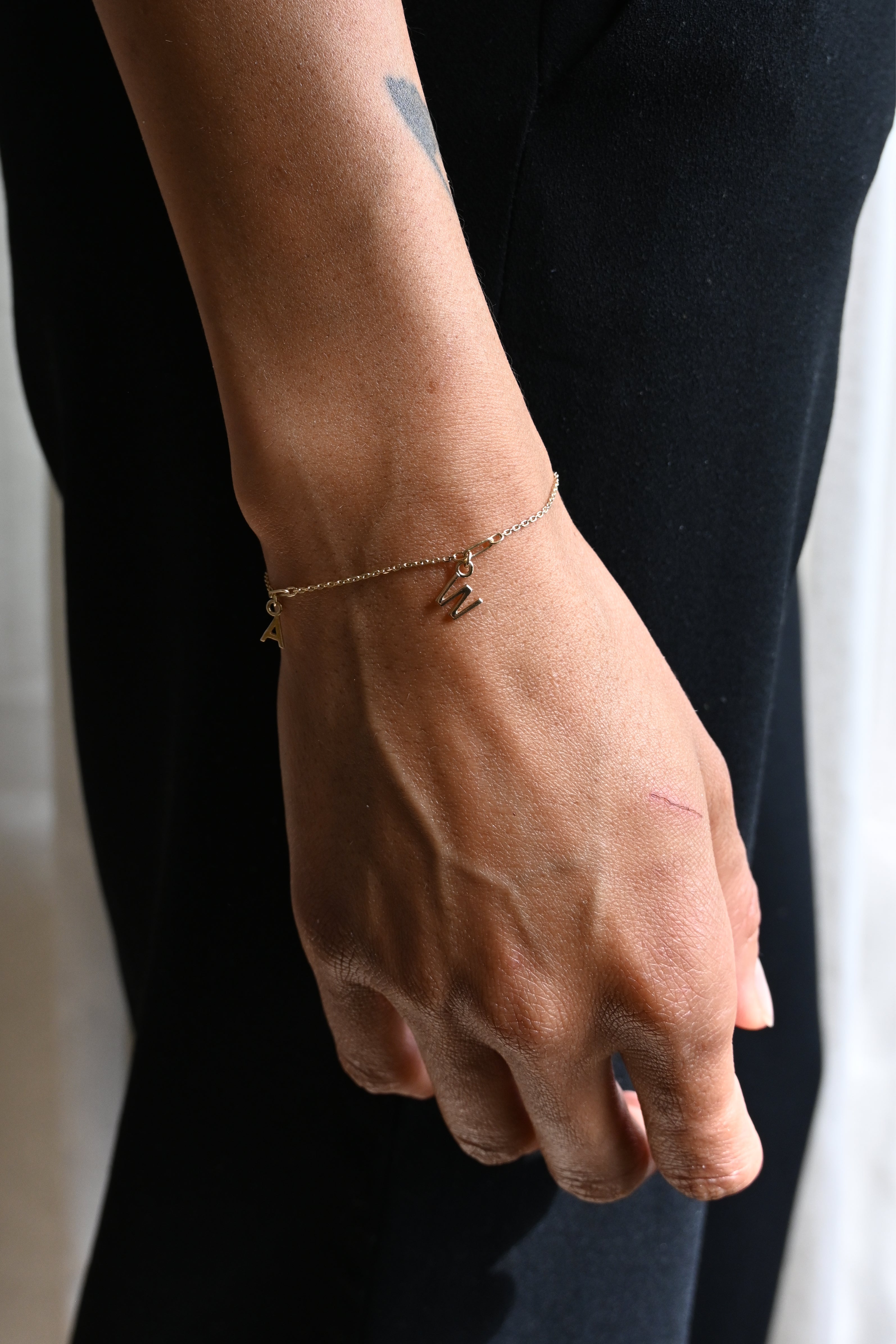 Image of models wrist, wearing a personalised gold bracelet with initial