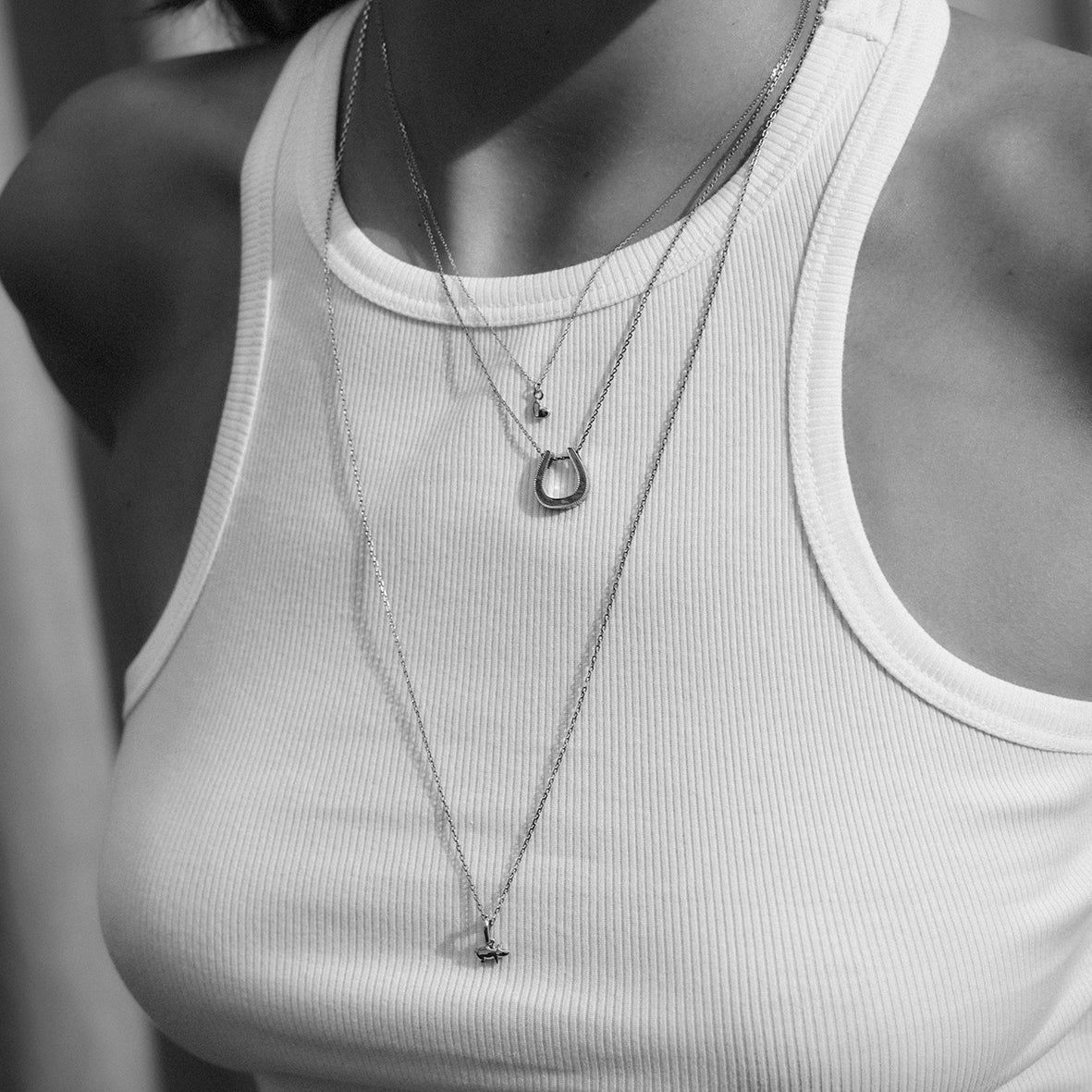 Person wearing a white tank top with layered gold necklaces