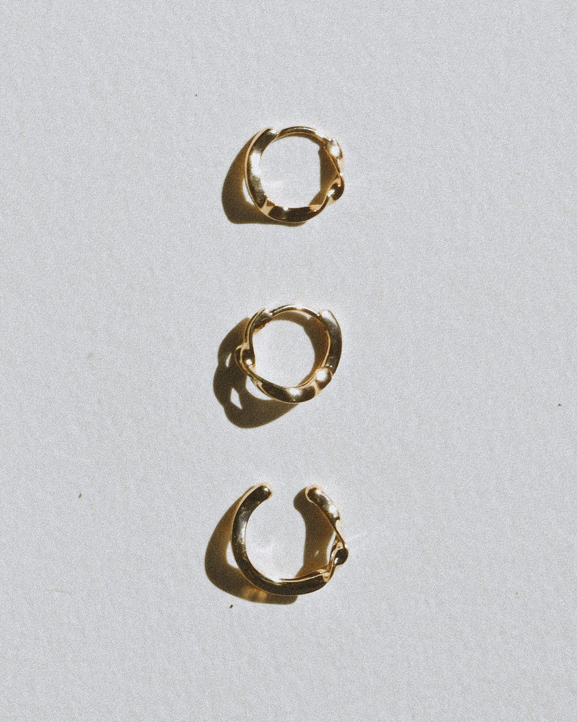 Three gold hoop earrings on a light gray background