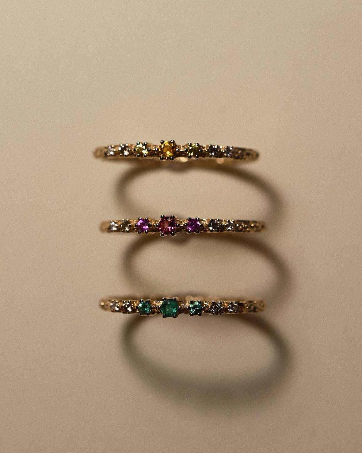 Three gold rings with embedded gemstones on a beige background