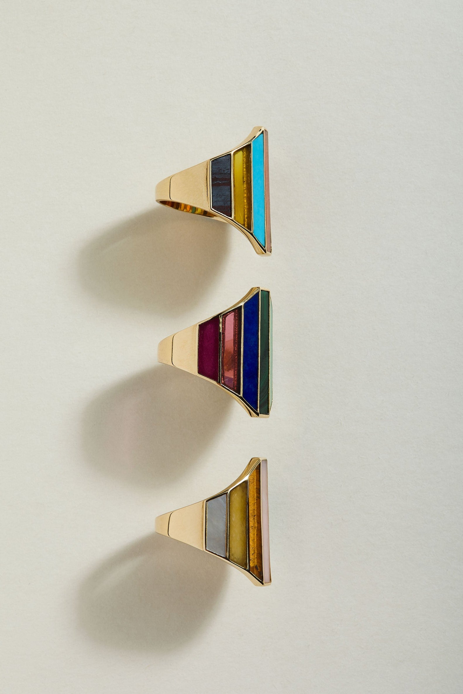 Three geometrically shaped rings with colorful inlay on a light gray background